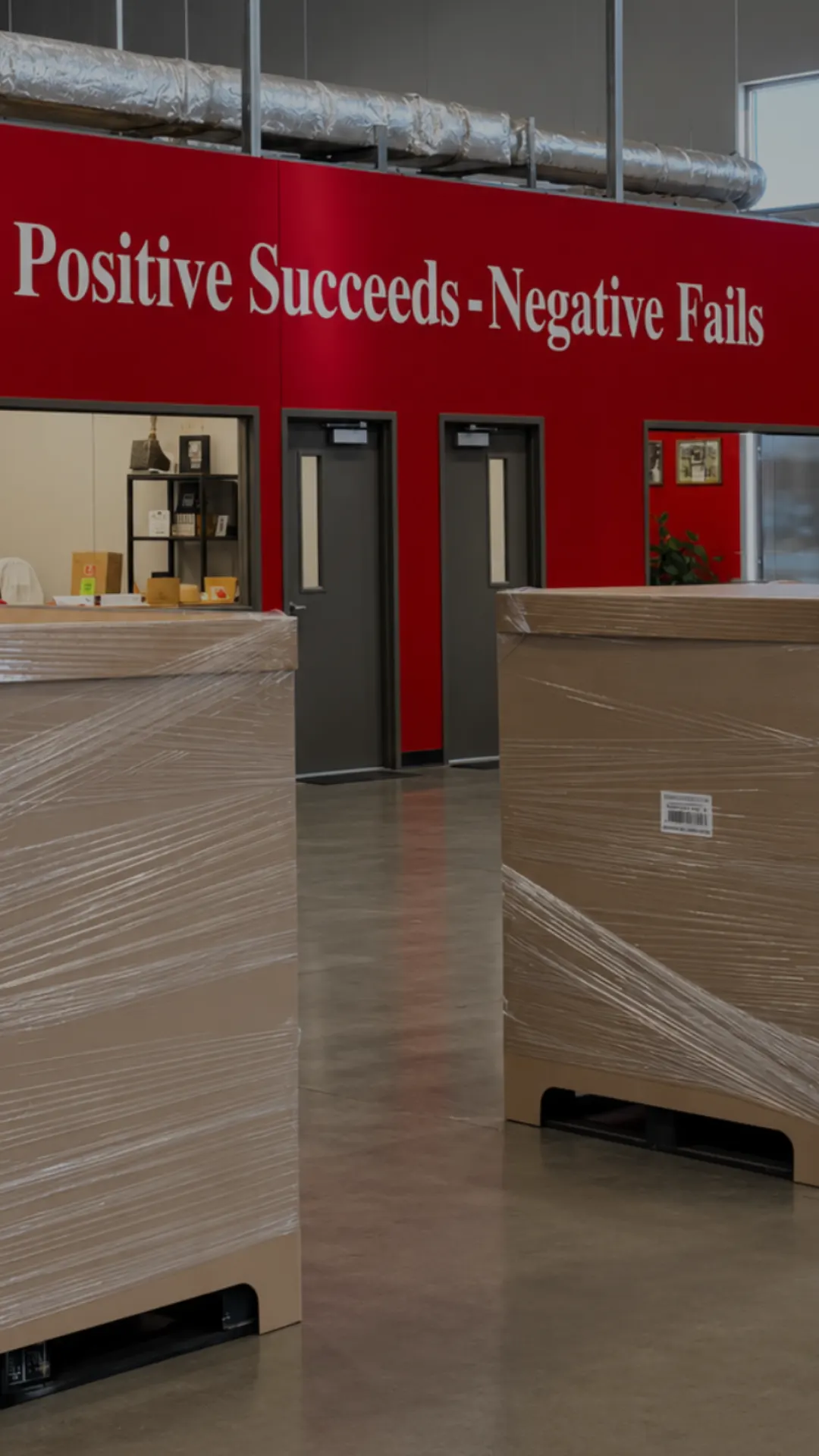 Shrink-wrapped pallets in front of the office wall reading Positive Succeeds - Negative Fails