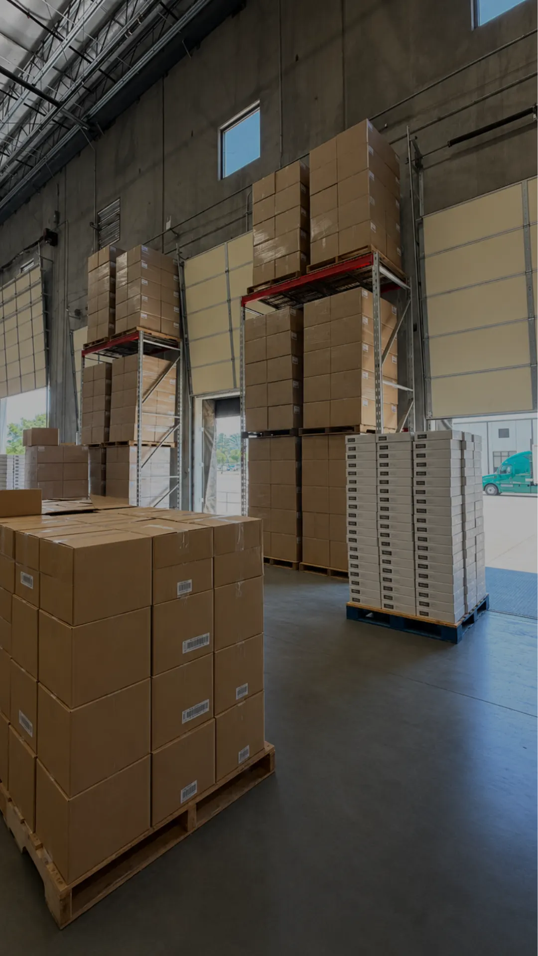 Palletized cases stacked high at the dock doors with a truck outside